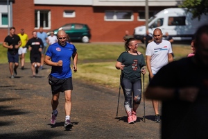 Jeden z uczestników biegnie, kobieta uczestnicząca idzie z nordic walking, a mężczyzna z nią idzie