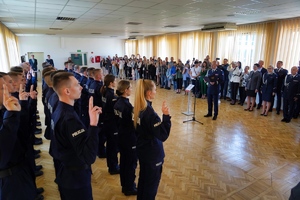 Nowoprzyjęci policjanci stojąc przed komendantem składają rotę ślubowania