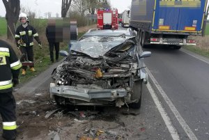 Miejsce zdarzenia drogowego. Na pierwszym planie rozbite renault. Za nim pojazd straży pożarnej, po prawej stronie przejeżdżający pojazd ciężarowy.