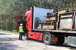 Zdjęcie przedstawia umundurowanego policjanta ruchu drogowego kontrolującego ciężarówkę.