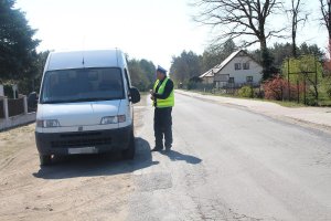 Zdjęcie przedstawia umundurowanego policjanta ruchu drogowego kontrolującego pojazd dostawczy.