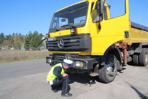 Zdjęcie przedstawia umundurowanego policjanta ruchu drogowego kontrolującego ciężarówkę.