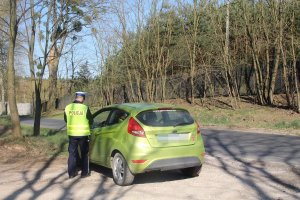 Zdjęcie przedstawia umundurowanego policjanta ruchu drogowego kontrolującego samochód osobowy.