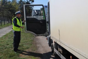 Zdjęcie przedstawia umundurowanego policjanta ruchu drogowego kontrolującego ciężarówkę.