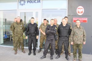 Fotografia przedstawia umundurowanych policjantów stojących przed budynkiem komisariatu policji w Szubinie wspólnie z przedstawicielami straży leśnej, straży rybackiej i straży łowieckiej.