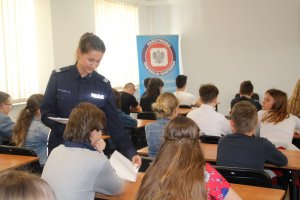 Fotografia przedstawia umundurowaną policjantkę rozdającą uczestnikom konkursu testy.