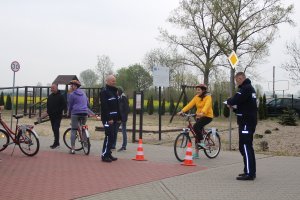 Dziewczynka jedzie rowerem po torze przeszkód a obok stoją policjanci