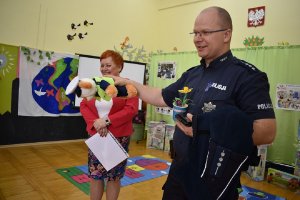 Na zdjęciu stoi policjant i trzyma w ręce maskotkę