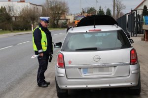 Zdjęcie przedstawia umundurowanego policjanta ruchu drogowego prowadzącego kontrolę stojącego przed nim auta.