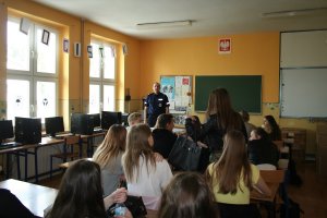 Zdjęcie przedstawia umundurowanego policjanta prowadzącego zajęcia dla siedzących przed nim uczniów.