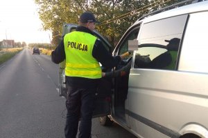 Zdjęcie przedstawia umundurowanego policjanta, dodatkowo ubranego w żółtą kamizelkę. Policjant prowadzi kontrolę trzeźwości kierowcy przejeżdżającego auta.