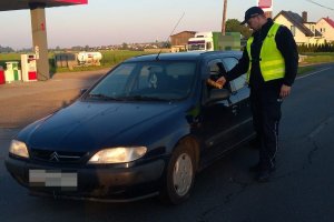 Zdjęcie przedstawia umundurowanego policjanta, dodatkowo ubranego w żółtą kamizelkę. Policjant prowadzi kontrolę trzeźwości kierowcy przejeżdżającego auta.