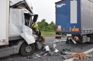 Zdjęcie przedstawia naczepę pojazdu ciężarowego koloru niebieskiego. za nią rozbity ciężarowy mercedes.