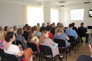 Zdjęcie przedstawia siedzących w ławkach uczestników spotkania.