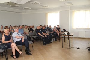 Zdjęcie przedstawia siedzących w ławkach uczestników spotkania. Wśród nich umundurowanych policjantów.