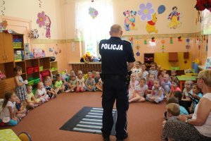 Zdjęcie przedstawia umundurowanego policjanta prowadzącego zajęcia dla przedszkolaków.