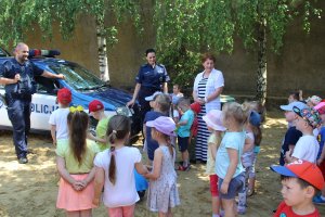 Zdjęcie przedstawia dzieci stojące obok radiowozów i słuchające umundurowanych policjantów. Na fotografii widoczne także opiekunki.