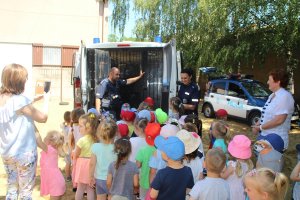 Zdjęcie przedstawia dzieci stojące obok radiowozów i słuchające umundurowanych policjantów. Na fotografii widoczne także opiekunki.