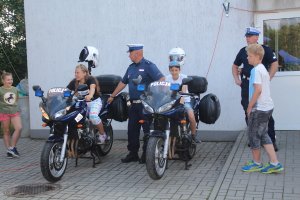 Zdjęcie przedstawia policjantów drogówki wraz z służbowymi motocyklami, obok policjantów stoją dzieci. na motorach siedzi dwoje dzieci.