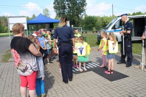 Zdjęcie przedstawia policjantów prowadzących pogadankę dla stojących przed nimi dzieci na temat bezpieczeństwa w ruchu drogowym.