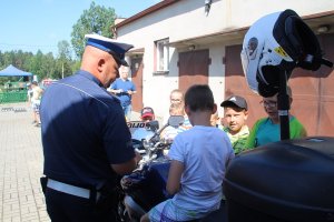 Zdjęcie przedstawia dziecko siedzące na policyjnym motocyklu. obok stoi umundurowany funkcjonariusz.