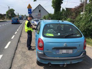 Zdjęcie przedstawia umundurowanego policjanta prowadzącego kontrole auta osobowego.