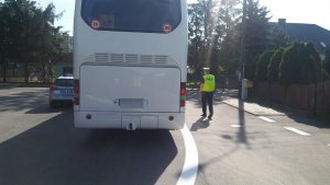 Zdjęcie przestawia policjanta ruchu drogowego kontrolującego stojący obok niego autokar.