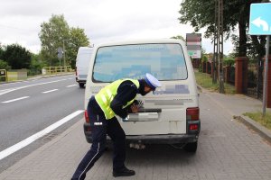 Zdjęcie przedstawia umundurowanego policjanta ruchu drogowego sprawdzającego sprawność oświetlenia kontrolowanego auta.