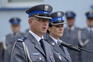 Zdjęcie przedstawia uroczystość Święta Policji - Komendant nakielskiej jednostki podczas przemowy. w tle lektor.