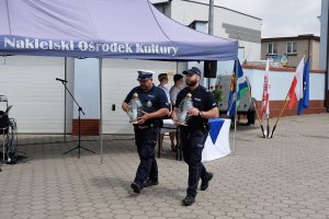 Zdjęcie przedstawia uroczystość Święta Policji - delegacja policjantów idzie ze zniczami, które złoży na grobach tragicznie zmarłych kolegów i pod Dębami pamięci o policjantach Policji Państwowej.