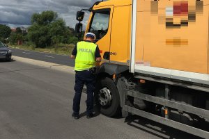 Zdjęcie przedstawia umundurowanego policjanta ruchu drogowego prowadzącego kontrolę auta ciężarowego