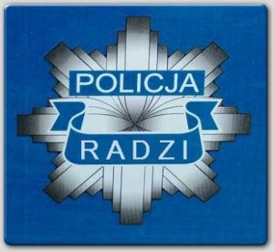 Zdjęcie przedstawia policyjną gwiazdę koloru szarego z napisami: POLICJA, RADZI. Tło zdjęcia niebieskie