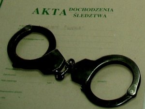 Zdjęcie przedstawia kajdanki ułożone na obwolucie akt postępowania