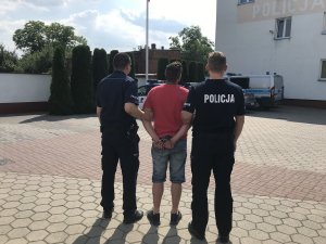 zdjęcie przedstawia umundurowanych policjantów prowadzących zatrzymanego mężczyznę.