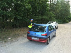 Zdjęcie przedstawia umundurowanego policjanta ruchu drogowego prowadzącego kontrolę auta.