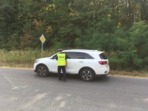 Zdjęcie przedstawia umundurowanego policjanta ruchu drogowego prowadzącego kontrolę trzeźwości kierowców aut.