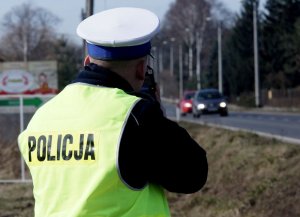 Zdjęcie przedstawia policjanta ruchu drogowego mierzącego prędkość pojazdów