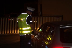 Zdjęcie przedstawia policjanta ruchu drogowego kontrolującego pojazd osobowy