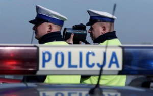 Zdjęcie przedstawia dwóch umundurowanych policjantów ruchu drogowego mierzących prędkość aut. na pierwszym planie radiowóz