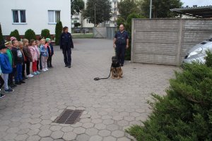 Zdjęcie przedstawia przewodnika policyjnego psa wraz z umundurowaną policjantką rozmawiających na placu komendy z dziećmi.