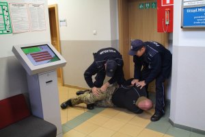 zdjęcie przedstawia dwóch umundurowanych policjantów obezwładniających agresora.