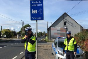 Zdjęcie przedstawia umundurowanych policjantów ruchu drogowego kontrolujących prędkość aut przemieszczających się trasą.