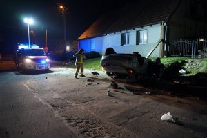 zdjęcie przedstawia rozbite auto uczestniczące w kolizji.  w tle widać strażaka oraz pojazd straży pożarnej.