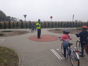 zdjęcie przedstawia policjanta prowadzącego zajęcia praktyczne dla uczniów na miasteczku ruchu drogowego.