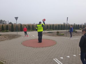 zdjęcie przedstawia policjanta prowadzącego zajęcia praktyczne dla uczniów na miasteczku ruchu drogowego.