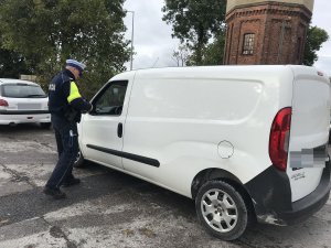 Zdjęcie przedstawia umundurowanego policjanta kontrolującego auto