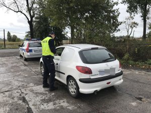 Zdjęcie przedstawia umundurowanego policjanta kontrolującego auto