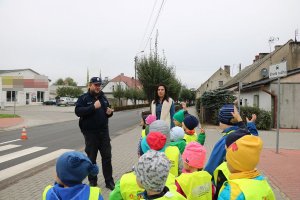 Zdjęcie przedstawia umundurowanego policjanta stojącego wspólnie z dziećmi w rejonie przejścia dla pieszych.