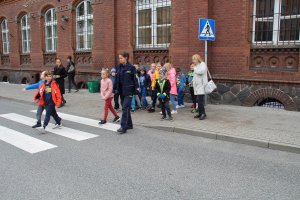 Zdjęcie przedstawia dzieci przechodzące wspólnie z umundurowaną policjantką przez przejście dla pieszych