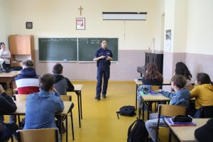 Zdjęcie przedstawia umundurowaną policjantkę prowadzącą w sali lekcyjnej zajęcia dla siedzących w klasie uczniów.